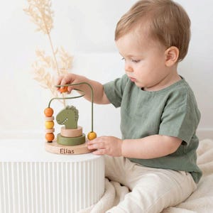 Peut inclure: Un jouet labyrinthe de perles en bois avec une t&ecirc;te de dinosaure verte, des perles orange et jaunes, et le nom "Elias" grav&eacute; sur la base. Le jouet a un cadre m&eacute;tallique pour faire glisser les perles. Con&ccedil;u pour les tout-petits.