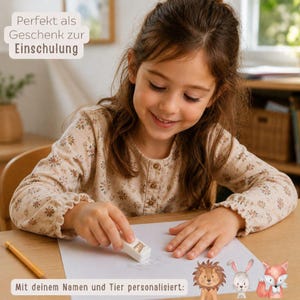 May include: A white rectangular eraser featuring a small animal illustration, positioned on a sheet of white paper. The eraser is personalised with a name and an animal graphic, including a lion, a rabbit, and a fox shown at the bottom.