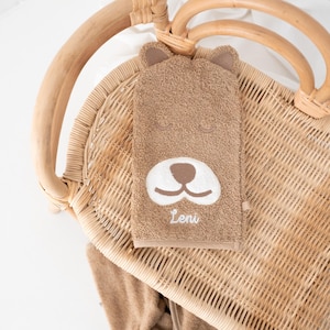 May include: A brown hooded towel with a bear face embroidered on the front. The towel has the name "Leni" embroidered below the bear's nose.