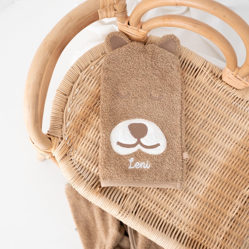 May include: A brown hooded towel with a bear face embroidered on the front. The towel has the name "Leni" embroidered below the bear's nose.