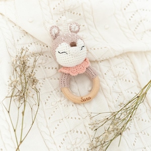 K&ouml;nnte beinhalten: Ein geh&auml;keltes Hirschr&auml;tsel mit einem rosa Kragen und einem Holzring. Der Ring ist mit dem Namen "Sara" graviert.