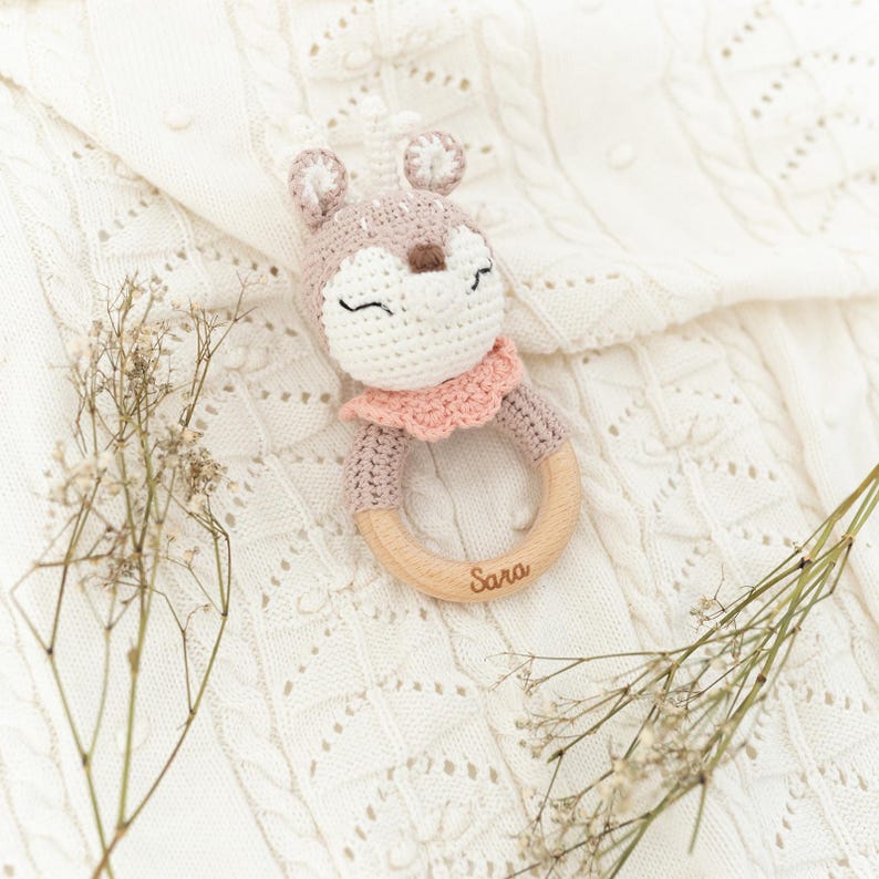 K&ouml;nnte beinhalten: Ein geh&auml;keltes Hirschr&auml;tsel mit einem rosa Kragen und einem Holzring. Der Ring ist mit dem Namen "Sara" graviert.