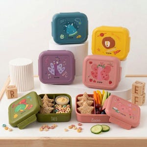 Könnte beinhalten: Eine Sammlung quadratischer Kunststoff-Lunchboxen in verschiedenen Farben wie Blaugrün, Gelb, Lila, Pink, Olivgrün und Hellrosa. Jeder Deckel zeigt eine einzigartige Tierillustration und den Markennamen Trixie. Zwei offene Boxen enthalten sternförmige Snacks, Obst und Gemüse.