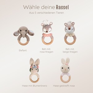 K&ouml;nnte beinhalten: F&uuml;nf geh&auml;kelte Babyrasseln mit verschiedenen Tierdesigns: Elefant, Reh mit rosa Kragen, Reh mit beigefarbenem Kragen, Hase mit Blumenkranz und gestreiftem Hasen. Der Text "W&auml;hle deine Rassel" und "Aus 5 verschiedenen Tieren" ist sichtbar.