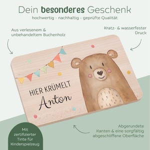 May include: A rectangular wooden board made of beech wood featuring a printed illustration of a brown bear, colorful bunting flags, and the German text "HIER KR&Uuml;MELT Anton". The board has rounded edges and a smooth, sanded surface finish.