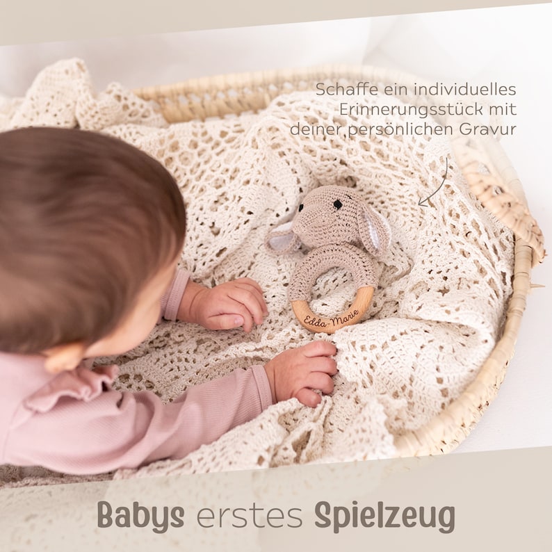 K&ouml;nnte beinhalten: Ein hellbraunes, geh&auml;keltes Hasenrassel mit einem Holzring. Der Ring ist mit dem Namen "Edda-Marie" graviert. Die Rassel befindet sich in einem Weidenkorb mit einer wei&szlig;en H&auml;keldecke.