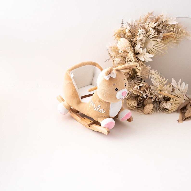 May include: A plush rocking animal toy shaped like a brown bunny with a white belly and pink accents. The toy has a wooden rocking base and is personalized with the name "Mila".