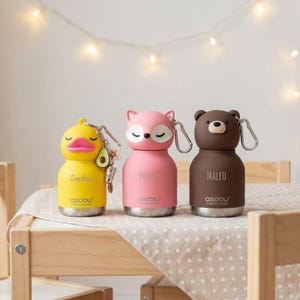 Pode incluir: Três garrafas de água isoladas em forma de pato, raposa e urso. A garrafa de pato amarela tem um bico rosa e o nome "Sophia". A garrafa de raposa rosa tem o nome "Noah". A garrafa de urso castanho tem o nome "Maleo". Todas as garrafas têm uma base prateada e um mosquetão.