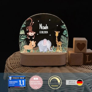 May include: A semi-circular acrylic night light with a wooden base, featuring a printed jungle scene with a monkey, lion, elephant, and giraffe. The text "Noah" and "17.08.2024" is printed in white. The light is dimmable and battery-operated.
