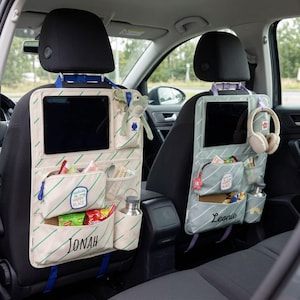Könnte beinhalten: Zwei beige und hellgrüne Auto-Rücksitz-Organizer mit diagonalen Streifen, Tabletfächern und mehreren Taschen. Ein Organizer trägt den Namen Jonah, der andere Leonie. Sie sind an den Sitzen befestigt und enthalten Snacks, Kopfhörer und Flaschen.