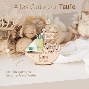 May include: A wooden sailboat with a &euro;100 note inside. The sailboat has a heart-shaped cutout and the text "Alles Gute zur Taufe" on the sail. The sailboat also has the text "SAMUEL 26.06.2024" on the bottom. The sailboat is surrounded by dried flowers.