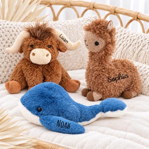 May include: Three plush stuffed animals: a brown highland cow with the name Luan on its horn, a brown llama with the name Sophia on its side, and a blue whale with the name Noah on its fin. Each toy features soft, textured fur and dark eyes.