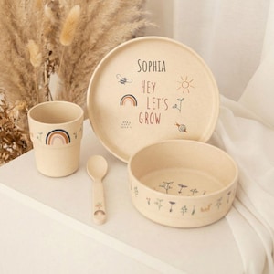 Könnte beinhalten: Ein beiges Kindergeschirr-Set mit einer Tasse, einem Teller, einer Schüssel und einem Löffel. Der Teller trägt den Namen "Sophia" und den Satz "Hey Let's Grow" mit Illustrationen von Regenbogen, Sonne, Biene und Schnecke.