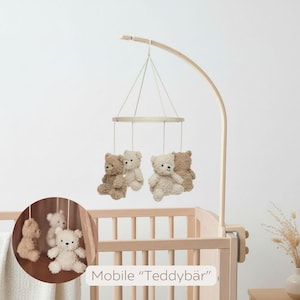May include: A baby crib mobile featuring four plush teddy bears in shades of beige and brown suspended from a wooden frame. The mobile is attached to a wooden arm. The text "Mobile 'Teddyb&auml;r'" is visible.