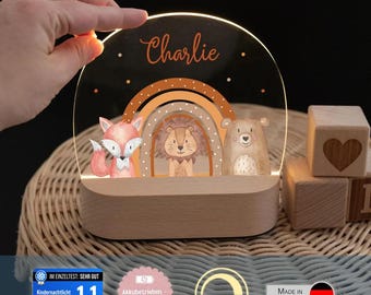May include: A semi-circular acrylic night light with a wooden base featuring a printed rainbow, a fox, a lion, and a bear. The name Charlie is printed at the top. The light is illuminated and displays a warm glow, showcasing a decorative design.