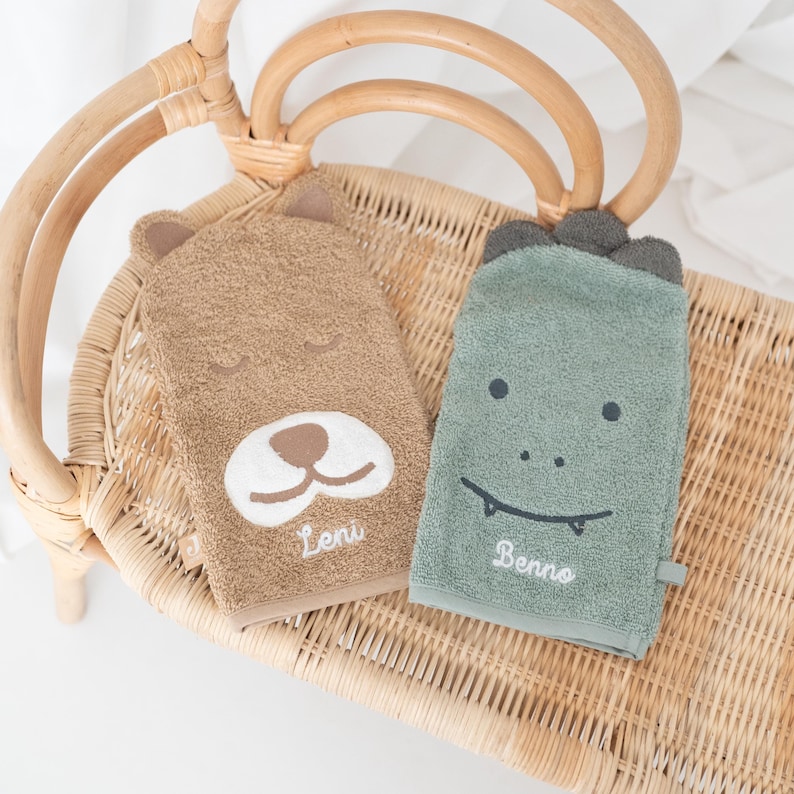 May include: Two plush hand towels with embroidered animal faces. The brown towel has a bear face with the name "Leni" embroidered below. The green towel has a dinosaur face with the name "Benno" embroidered below.