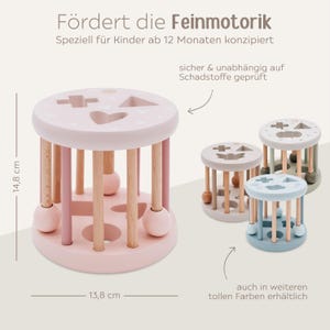 May include: Pink wooden toy with a rolling cylinder and colorful balls. The toy has different shaped cutouts on the top and is designed to help develop fine motor skills. The toy is 14.8 inches tall and 13.8 inches wide.
