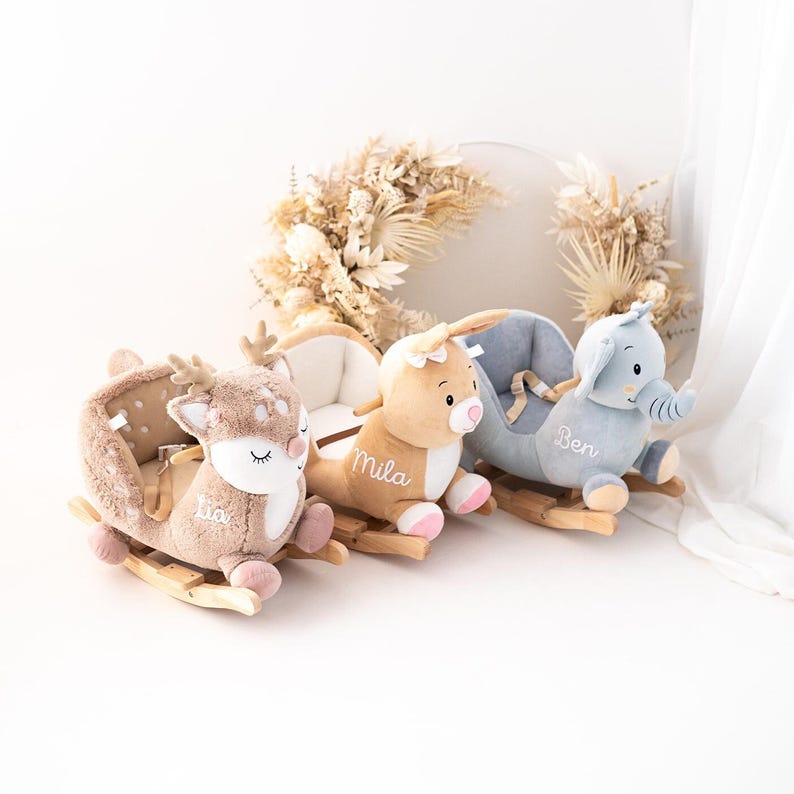 May include: Three plush rocking animals for children. A light brown deer with the name "Lia" embroidered on it, a light brown bunny with the name "Mila" embroidered on it, and a light blue elephant with the name "Ben" embroidered on it.