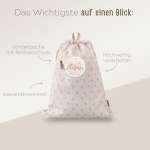 May include: A beige drawstring backpack with a floral pattern and the name "Riley" on a circular patch. The bag has a front zippered pocket and is labeled as water-repellent.