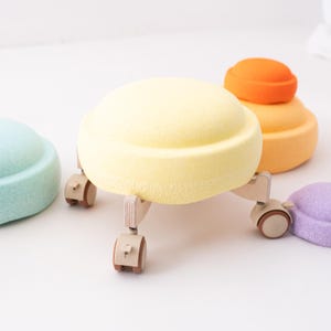 Può includere: Un set di quattro sedie rotonde, morbide e imbottite di colori vivaci con gambe in legno e ruote. Le sedie sono gialle, arancioni, blu chiaro e viola.