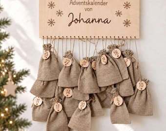 以下が含まれることがあります： Adventskalender von Johannaという文字と雪の結晶が刻印された長方形の木製看板。看板からは24個の薄茶色の麻袋が吊り下げられており、それぞれの袋は紐で結ばれ、小さな木製のタグが付いています。