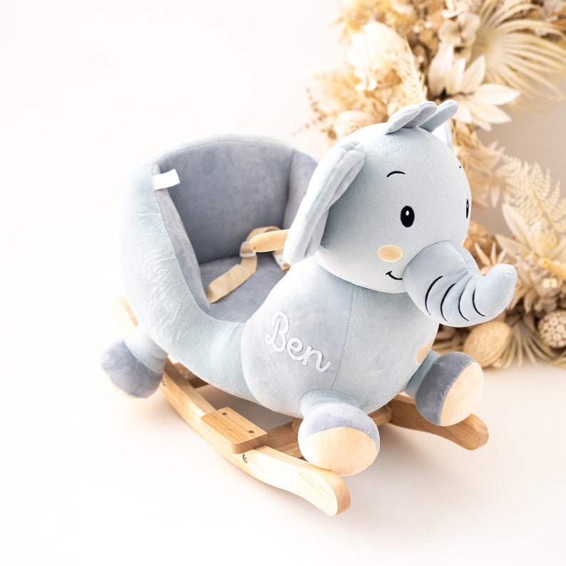 May include: A light blue plush rocking elephant with a wooden base. The elephant has a saddle and a safety harness. The elephant is embroidered with the name "Ben".