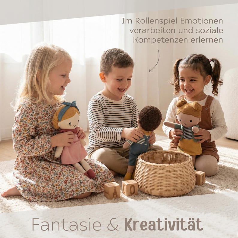 May include: Three children are smiling and playing with fabric dolls. The dolls have different skin tones and outfits. A woven basket and wooden blocks with letters are also in the image. Text at the top reads, "Im Rollenspiel Emotionen verarbeiten und soziale Kompetenzen erlernen." Text at the bottom reads, "Fantasie & Kreativit&auml;t."