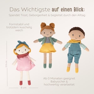 May include: Three soft fabric dolls. The doll on the left is wearing a pink dress and a red scarf. The middle doll has a yellow skirt and green jacket. The doll on the right has blue overalls and a yellow scarf. The dolls are 39 cm tall and 8 cm wide.