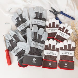 Może przedstawiać: Kolekcja rękawic roboczych w kolorach szarym, białym i brązowym, z napisami "CHEF-HANDWERKER BASTI", "BESTER PAPA", "JUNIOR-HANDWERKER THEO" i "PAPAS KLEINER HELFER". Widoczny jest również czerwony śrubokręt i niebieskie szczypce.