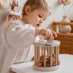 May include: A child plays with a wooden toy with a gray base and wooden dowels. The toy has a variety of shapes and colors. The toy is personalized with the name "Anni".