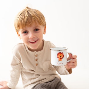 Puede incluir: Una taza de esmalte blanco con borde plateado que presenta una ilustraci&oacute;n estilo acuarela de un le&oacute;n y el nombre Levi impreso en letra roja. La taza tiene un asa en el lado derecho y se muestra sobre un fondo blanco liso.