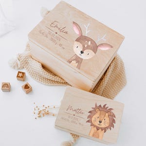 Puede incluir: Dos cajas de madera rectangulares con ilustraciones impresas de un ciervo y un le&oacute;n. La caja m&aacute;s grande muestra el nombre Emilia, una fecha y detalles de nacimiento. La caja m&aacute;s peque&ntilde;a muestra el nombre Matteo, una fecha y detalles de nacimiento.