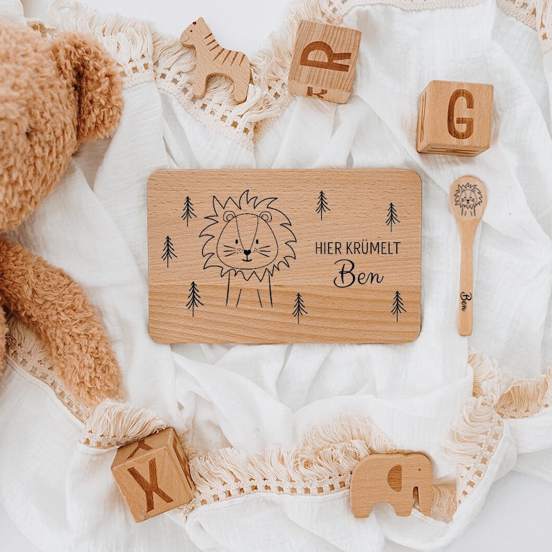 May include: A wooden plate with a lion illustration and the text "HIER KRUMELT Ben". The plate is surrounded by wooden toys, including a giraffe, elephant, and blocks.