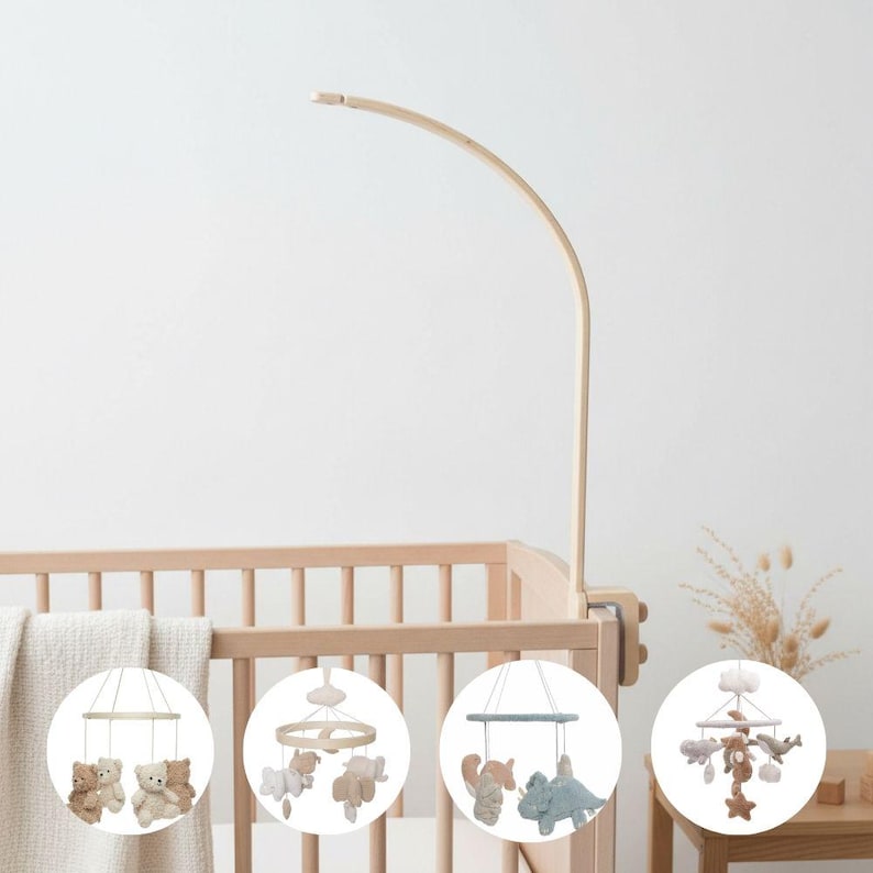 May include: A wooden baby crib mobile with a curved arm, attached to the crib. The mobile features four different designs: teddy bears, clouds and stars, woodland animals, and sea creatures. The crib is made of light-colored wood.