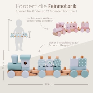 May include: Wooden toy train set in pastel blue, pink, and natural wood tones. The train is 31.5 cm long and 12 cm high. The text says it is designed for children 12 months and up.