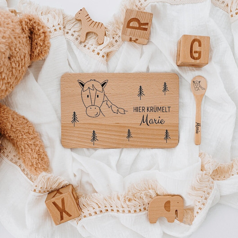 May include: Wooden plate with a horse illustration and the text "Hier kr&uuml;melt Marie". The plate is surrounded by wooden toys, including a zebra, elephant, and blocks.
