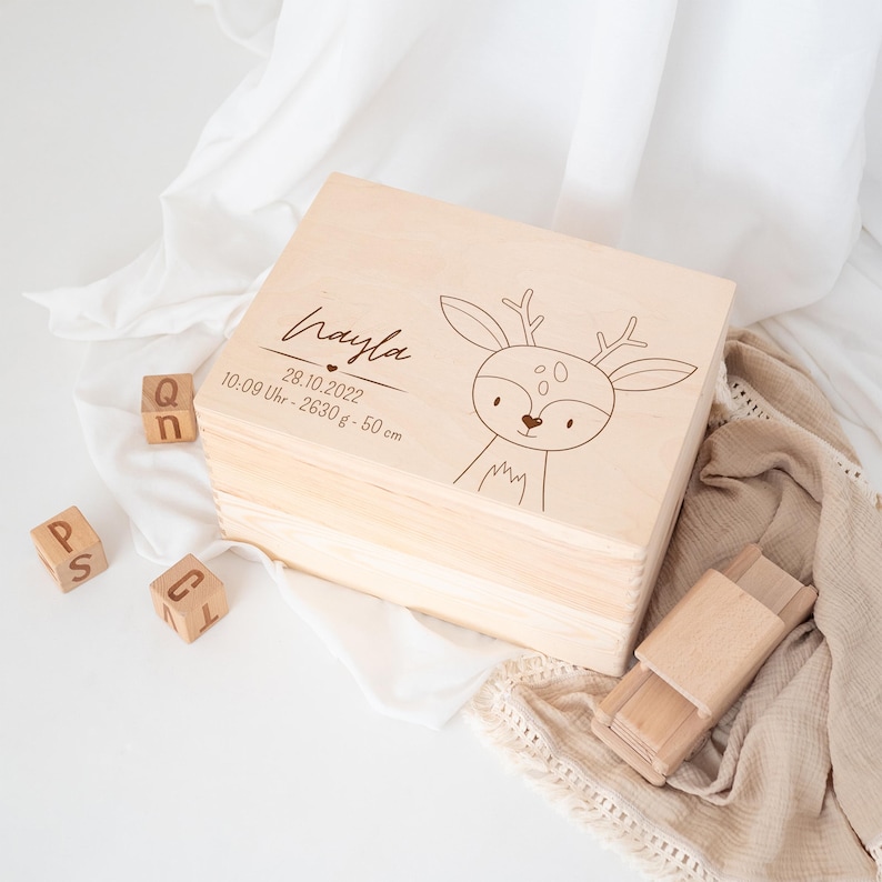 May include: A wooden keepsake box with a deer design and the name "Nayla" engraved on the lid. The box also includes the date "28.10.2022", time "10:09 Uhr", weight "2630g", and length "50 cm".