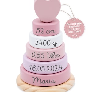 Może przedstawiać: Drewniana zabawka do układania w stosy w odcieniach r&oacute;żu, bieli i naturalnego drewna, zwieńczona sercem. Zabawka zawiera wymiary 52 cm, 3400 g i imię "Maria". Etykieta głosi: "Idealny prezent na narodziny lub chrzest."