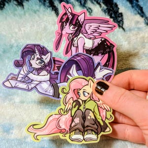 May include: Three die-cut vinyl stickers featuring stylized cartoon ponies. One purple pony with wings stands, a second purple pony with a white coat and phone lies down, and a third yellow pony with pink hair and wings sits wearing a green hoodie.