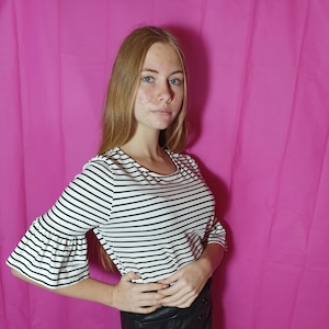 May include: A woman wearing a black and white striped shirt with bell sleeves and a black leather skirt.