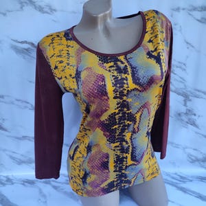 May include: A long-sleeved shirt with a snakeskin pattern in shades of yellow, purple, and gray. The sleeves are a solid maroon color.