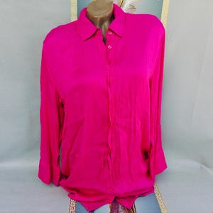May include: A vibrant fuchsia-colored button-down shirt with long sleeves. The shirt features a classic collar and buttoned cuffs. The fabric has a subtle sheen, suggesting a silky or satin-like material. The shirt is displayed on a mannequin.