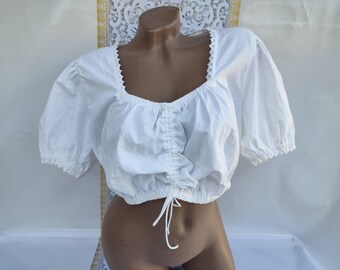 May include: A white peasant top with a gathered neckline and short puff sleeves. The top has a lace trim around the neckline and is tied at the waist.