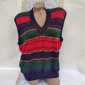 Puede incluir: Un chaleco de punto a rayas con cuello en V. El chaleco está hecho de un material suave y cálido y presenta un patrón colorido de rayas rojas, verdes, azules y amarillas.