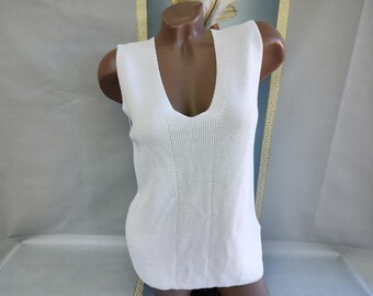 May include: White sleeveless sweater with a deep V-neck. The knit top has a ribbed texture with vertical and diagonal patterns. The garment is displayed on a mannequin. The overall style is classic and versatile.