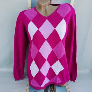 May include: A magenta V-neck sweater with a classic argyle pattern in shades of pink and white. The long-sleeved sweater is displayed on a mannequin, showcasing the diamond design. This knitwear piece is suitable for casual or semi-formal wear.