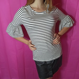 May include: A white and black striped shirt with a ruffled sleeve. The shirt is tucked into a black skirt.