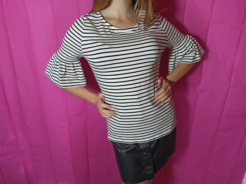 May include: A white and black striped shirt with a ruffled sleeve. The shirt is tucked into a black skirt.