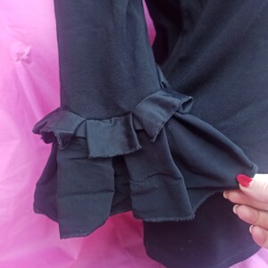 May include: Black blouse with ruffled sleeves. The sleeves have a layered, frilled design.