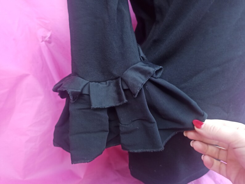 May include: Black blouse with ruffled sleeves. The sleeves have a layered, frilled design.